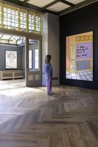 Gallery view with visitor observing Robbie Williams' large yellow and purple text piece at Moco Museum Amsterdam.